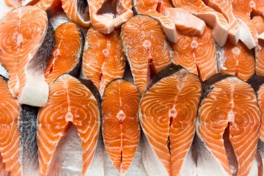 Vibrant salmon fillets are neatly arranged on a bed of ice showcasing their bright orange color and marbling. The market atmosphere is lively attracting customers ready to purchase fresh seafood.