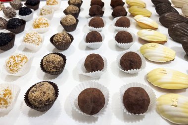 Colorful handmade candies and chocolates are neatly arranged on a white table. Various shapes and flavors are present showcasing a delightful selection perfect for celebrations or casual enjoyment.