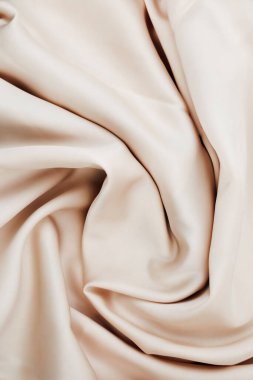 Luxurious beige fabric drapes elegantly with soft folds and a smooth surface. Ideal for clothing upholstery or home decor projects showcasing a timeless and versatile color.