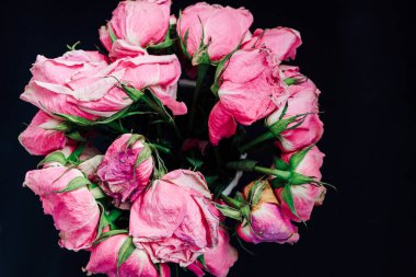 A round bouquet of dried pink roses displays their faded beauty against a dark background. The petals show signs of aging while still highlighting their delicate shape and vibrant color.