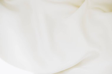 A delicate soft white fabric rests gracefully on a smooth light colored surface. Gentle folds and textures create a serene and airy atmosphere enhanced by natural lighting.