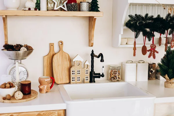 Noel mutfağı dekorasyonunda zencefilli kurabiye evleri ve kozalaklar da yer alıyor. Raflar pişirme malzemeleri taşırken, beyaz bir lavabo ve tahta kesme tahtaları uzaya cazibe katıyor..