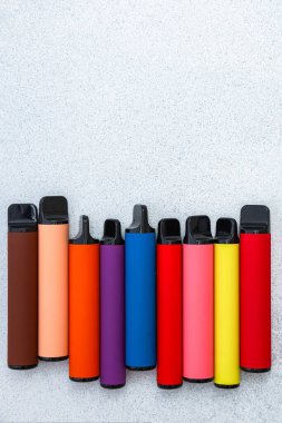 Gri arka planda renkli elektronik sigara çeşitleri. Farklı renklerde modern buharlaştırma cihazlarının çeşitliliği, minimalist bileşim, nikotin alternatifleri, teknoloji ve yaşam tarzı kavramı