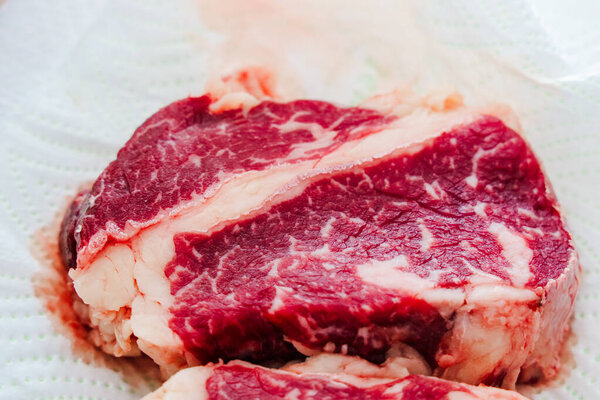 Thick cut of red beef steak sits on a paper towel in a kitchen. The marbling shows high quality meat prepared for grilling or pan searing. This cut is ideal for a hearty meal or barbecue.