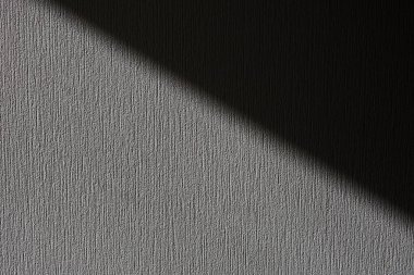 Yumuşak bir ışık, dokulu bir duvara keskin bir gölge düşürür aydınlık ve karanlığın şaşırtıcı bir kontrastını yaratır. Bu sahne, basit bir tasarımın güzelliğini sessiz bir mekanda yakalıyor ve dokuyu vurguluyor..