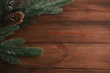 Green pine branches and a pine cone are arranged on a rustic wooden table creating a warm festive atmosphere. This cozy scene evokes the spirit of the holiday season perfect for decorating.