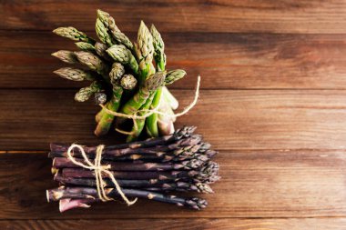 A vibrant display of green and purple asparagus tied with twine sits on a rustic wooden table. This fresh produce is perfect for healthy meals and seasonal recipes.