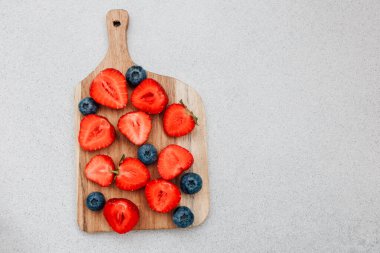 Bright red sliced strawberries and fresh blueberries are artfully arranged on a wooden cutting board. This vibrant display is perfect for a healthy snack or summer dessert.