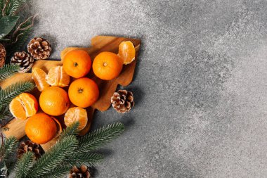 Portakallar, çam kozalakları ve yeşil dallarla çevrili ağaç şeklinde tahta bir tahtanın üzerine konur. Sahne, şenlikli dekorasyon için düzenlenmiş kış eşyaları koleksiyonunu gösteriyor..