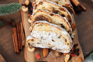 Çalıntı kek dilimleri, ceviz ve kurumuş meyvelerle çevrili bir tahtanın üzerinde oturur. Sahne, tatil sezonunda etrafındaki baharatlarla şenlikli bir atmosfer öneriyor..