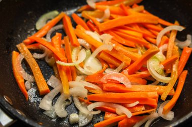 Havuç ve soğan ince dilimlere ayrılır ve kızartma tavasında birlikte pişirilir. Soba, bu sebzeleri yemeğe hazırlamak için kullanılıyor. Bu, akşam vakti bir mutfakta gerçekleşir..