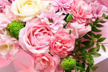 Bir çiçek koleksiyonu pembe beyaz ve yeşil tonlarda birlikte düzenlenir. Bukette güller ve daha küçük çiçekler var. Bu düzenleme bir masanın üzerindeki vazoya konur..