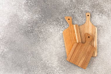 Gri taştan bir yüzeye üç tahta kesme tahtası yerleştirilir. Tahtalar boyut ve şekil olarak değişir. Sebze doğramaya ya da mutfak ortamında yemek hazırlamaya hazırlar..