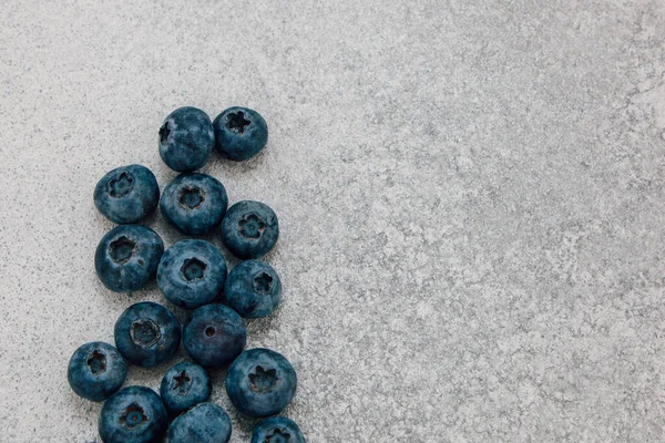 Yabanmersini gri bir taş yüzeyde dağılmış. Meyve koyu mavi rengini ve yuvarlak şeklini gösterir. Bu ayar gıda gösterimi veya yemek tarifi kullanımı için doğal ve basit.