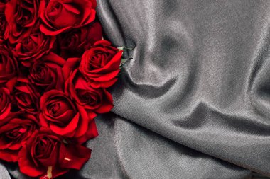 Kırmızı güller gri kumaşın yanında düzenlenir. Kumaşın pürüzsüz bir dokusu var. Doğal ışık yapraklara vurgu yapıyor. Bu sahne aşkı ya da kutlamayı temsil edebilir. Renkler birbiriyle zıtlaşıyor.
