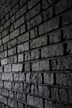 Karanlık tuğlalarla örülmüş bir duvar dar bir alanda duruyor. Tuğlalar dokuyu ve detayı gösteriyor. Düşük ışık bu ayardaki düzensiz yüzeyleri ve gölgeleri vurgular.