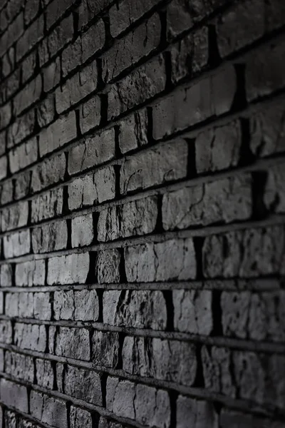 Karanlık tuğlalarla örülmüş bir duvar dar bir alanda duruyor. Tuğlalar dokuyu ve detayı gösteriyor. Düşük ışık bu ayardaki düzensiz yüzeyleri ve gölgeleri vurgular.