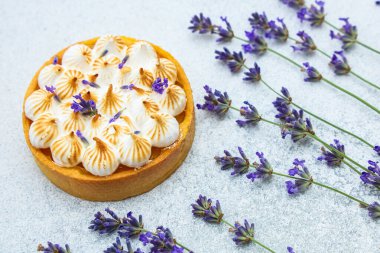 Yuvarlak bir tart açık bir yüzeyde sergilenir. Turtanın kremalı kremalı ve kıvrımlı desenleri var. Taze lavanta çiçekleri tartın yanına yerleştirilir ve olay yerine renk ve detay eklenir..