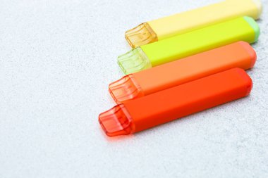 Renkli vapurlar, açık bir yüzeyde sıralanmış elektronik sigaralar, sarı yeşil turuncu ve kırmızı.