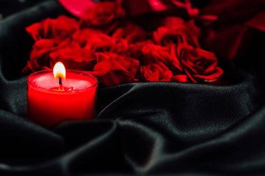 Kırmızı bir mum, bir akşam toplantısında ya da yas tutarken koyu bir örtüye dizilmiş bir demet taze kırmızı gülün yanında parlar.