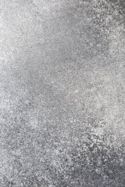 Değişen doku ve aşınma şekillerini gösteren gri bir yüzeye yakından bakmak. Işık, pürüzsüz ve pürüzsüz bölgelerini vurguluyor. Arka plan sade..