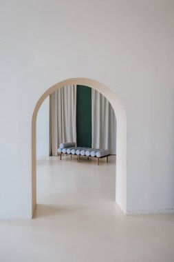 Kemer yolu manzarası oturma alanı ve perdeleri olan bir odayı ortaya çıkarır. Mekanın açık renkli duvarları ve basit mobilyaları olan minimalist bir tasarımı var. Doğal ışık odayı dolduruyor..