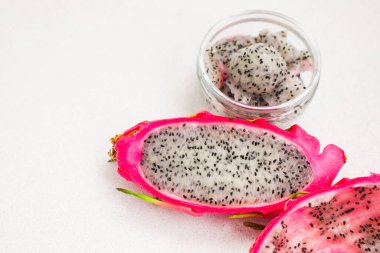 Dilimlenmiş taze bir ejderha meyvesi beyaz etini siyah tohumlarla sergiler. Küçük bir cam kapta daha fazla ejderha meyvesi küpü var..