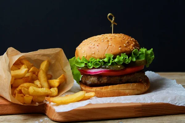 Siyah arka planda tahtadan yapılmış patates kızartmalı taze lezzetli burger. Yan Görünüm.