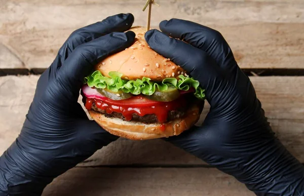 Burger Saboroso Fresco Segurando Mãos Luvas Pretas Fundo Madeira Vista — Fotografia de Stock