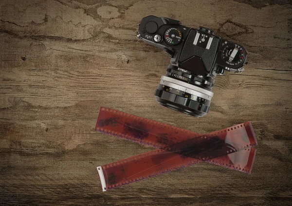 Fotoaparát a fotografické 35 mm filmový pás na dřevěné pozadí — Stock fotografie