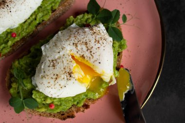 Üst manzara: Pembe tabakta taze avokado kreması üzerine sıvı sarısı ile kesilmiş haşlanmış yumurta. Bıçağın sapında yumurta sarısı