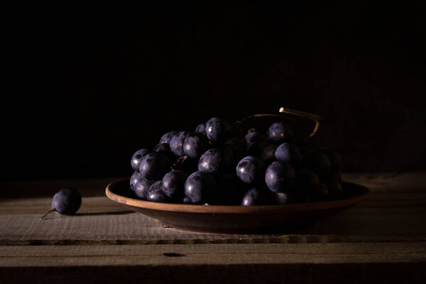 Ripe bunch of red grapes on a clay plate on a wooden rustic table, shot in low key