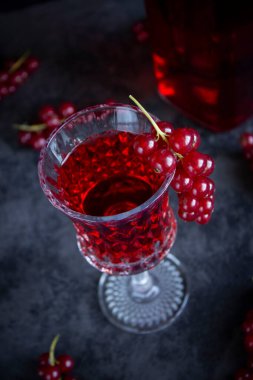 Gri bir çimento yüzeyinde güzel bir cam kadehte kırmızı frenk üzümü içeceği. Açılı camda bir demet kırmızı frenk üzümü.