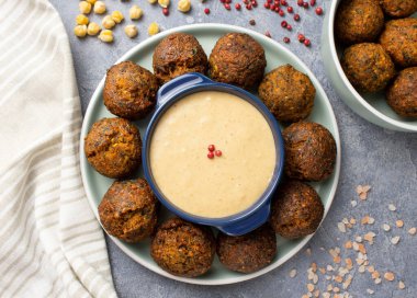 Falafel 'in üst görüntüsü, ortasında sos olan naneli bir tabakta daire şeklinde serilmişti. Pembe biber, pembe himmalay tuzu, nohut, keten havlu ve beton gri yüzeyde bir kase falafel.