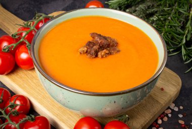 Tahta servis tahtasındaki yeşil bir kasede salamura vejetaryen otuzbircilerle domates kremalı çorba. İçindekiler: kiraz domatesleri, otlar, tuz - tahtaya yayılmış.