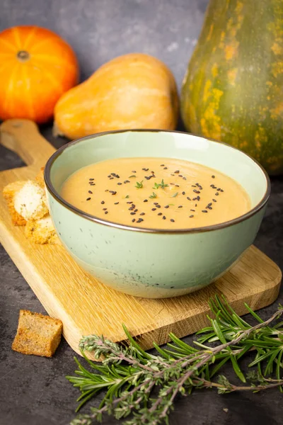 Pumpkin cream soup in a green bowl with black sesame seeds and thyme leaves on a wooden board