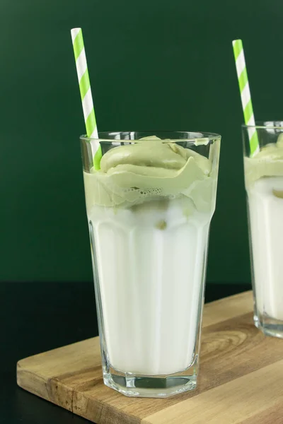 Whipped green matcha tea with milk and iced in a tall glass with a paper straw. Dalgona matcha trendy drink