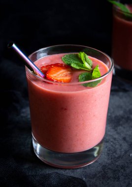 Yeşil nane yapraklı bir bardakta çilekli smoothie, çilek dilimleri ve düşük tuşlu metal bir tüp.