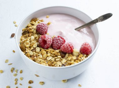 Ahudududulu yoğurt, granola ve donmuş ahududu beyaz bir yüzey üzerinde seramik kasede.