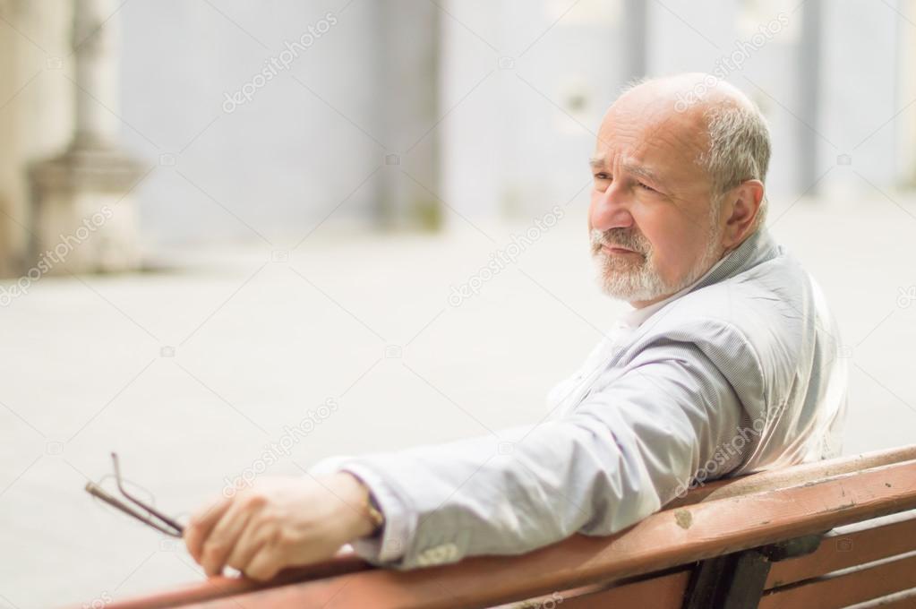 respectable elderly man sitting on a bench on the background of the city