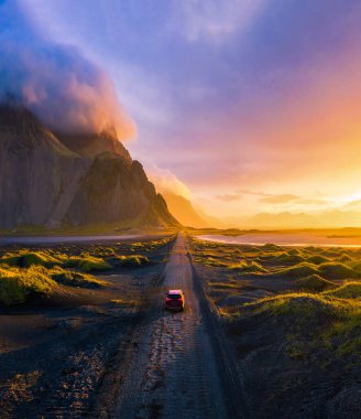 Gravel road at sunset with Vestrahorn mountain and a car driving, Iceland clipart