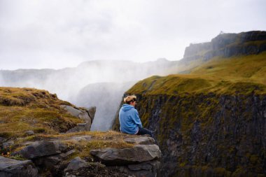 İzlanda 'da Gullfoss şelalesinin kenarında oturan yürüyüşçü.