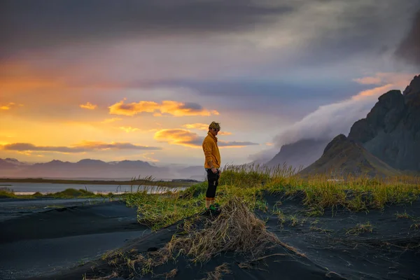 O turista fica em uma duna de areia na montanha Vestrahorn, na Islândia, ao pôr do sol — Fotografia de Stock