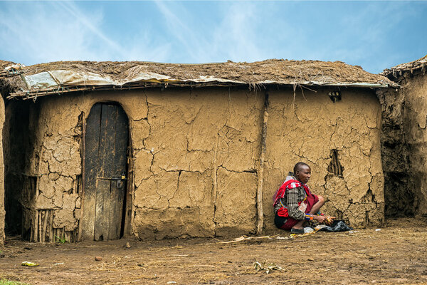 MASAI MARA, KENYA - OCTOBER 17, 2014: African woman from Masai tribe working in front of her village house. The Maasai are a Nilotic ethnic group living in southern Kenya and northern Tanzania