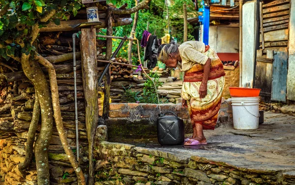 Muy vieja mujer encorvada llena un bidón con agua — Foto de Stock