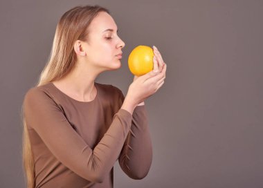 Genç ve güzel bir kız elinde portakal portakalı tutuyor ve kokusunu alıyor..