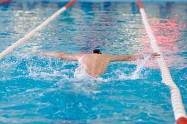 Bir yüzücü havuzda antrenman yaparken kollarını sallıyor, bulanıklaşıyor.