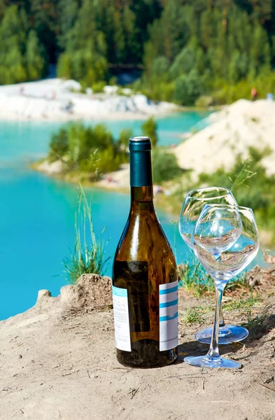 A bottle of wine and glasses on the shore of the blue Bay. The concept of a holiday and a picnic and a romantic evening at the sea on a hot sunny day.