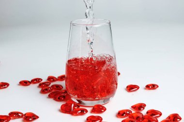Sevgililer Günü. Bir bardak suda küçük kırmızı cam kalpler. Bir damla sıvı..