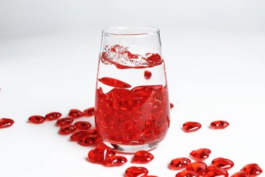 Sevgililer Günü. Bir bardak suda küçük kırmızı cam kalpler. Bir damla sıvı..